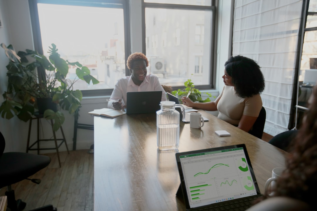 A diverse group of entrepreneurs working on laptops in a modern co-working space with success metrics and growth charts visible on screens