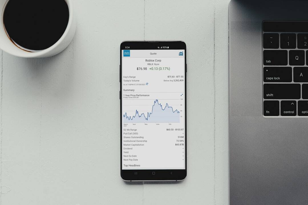 a smartphone displaying investment app charts and graphs next to a cup of coffee on a clean desk